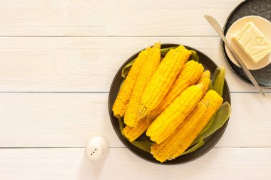 Lezzetli, sulu, kaynamış mısır beyaz ahşap arka planda bir tabakta, tereyağı ve tuzla pişirilmiş mısır koçanı.