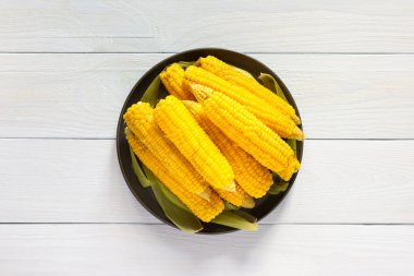 Lezzetli, sulu, kaynamış mısır, beyaz ahşap arka planda bir tabakta, mısır koçanı pişirilmiş.