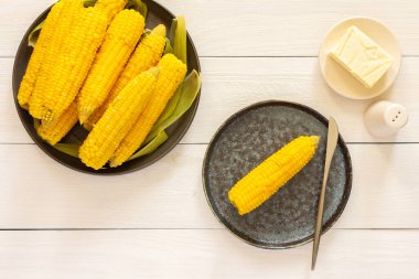 Lezzetli, sulu, kaynamış mısır beyaz ahşap arka planda bir tabakta, tereyağı ve tuzla pişirilmiş mısır koçanı.