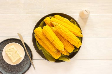 Lezzetli, sulu, kaynamış mısır beyaz ahşap arka planda bir tabakta, tereyağı ve tuzla pişirilmiş mısır koçanı.