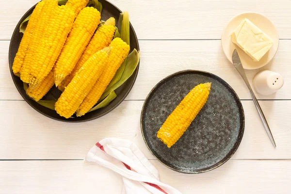 Lezzetli, sulu, kaynamış mısır beyaz ahşap arka planda bir tabakta, tereyağı ve tuzla pişirilmiş mısır koçanı.