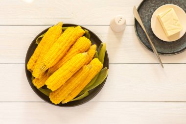Lezzetli, sulu, kaynamış mısır beyaz ahşap arka planda bir tabakta, tereyağı ve tuzla pişirilmiş mısır koçanı.