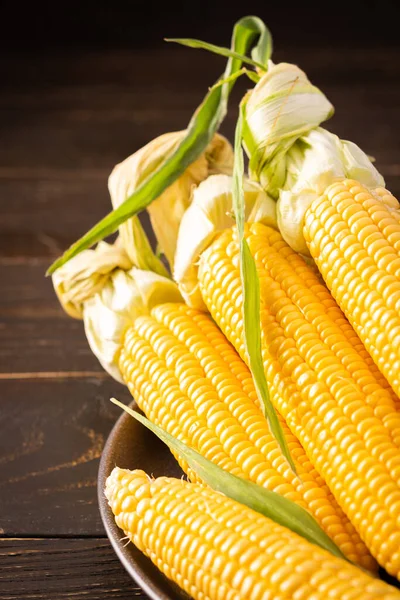 Taze mısır, organik mısır koçanı ve koyu ahşap arka planda yapraklar.