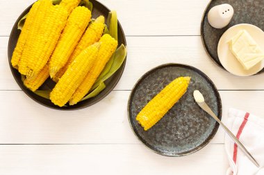Lezzetli, sulu, kaynamış mısır beyaz ahşap arka planda bir tabakta, tereyağı ve tuzla pişirilmiş mısır koçanı.