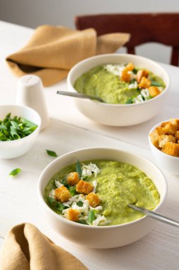 Sağlıklı lezzetli brokoli ve mozarella soslu salatalık kremalı çorba, yeşil soğan ve kızarmış ekmek, beyaz bir masada çorba.