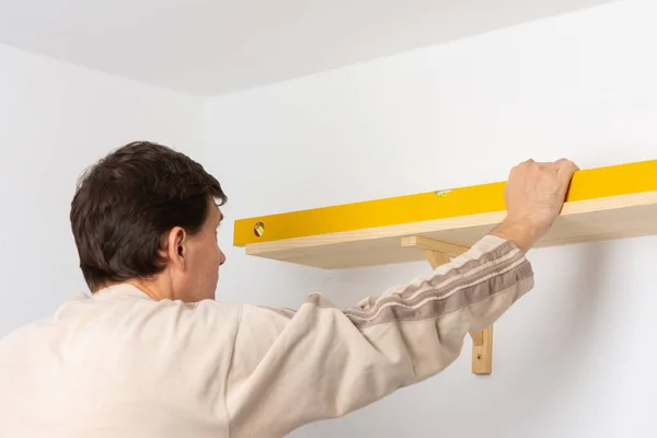 Beyaz bir duvardaki bir dairede bir adam rafı asıyor, bir işçi sabitleyici ile rafın akşam olup olmadığını kontrol ediyor.