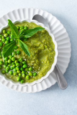 Bir kase canlı yeşil bezelye ve brokoli çorbası lezzet için taze nane yapraklarıyla kaplıdır. Bu sağlıklı yemek sıcak bir öğle yemeği ya da evde sıcak bir akşam yemeği için mükemmel.
