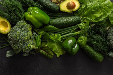 Brokoli, salatalık, yeşil biber, marul, fesleğen ve dereotu gibi yeşil sebzelerin yanı sıra olgun avokado gibi çeşitli yeşil sebzeler koyu bir arka planda, sağlıklı bir yemekte ustalıkla düzenlenmiştir.