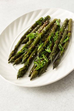 Taze otlarla kaplı buharda pişirilmiş kuşkonmaz, beyaz bir tabakta güzelce sıralanır. Yemek canlı görünüyor ve sağlıklı bir yemek ya da yan yemek için uygun..