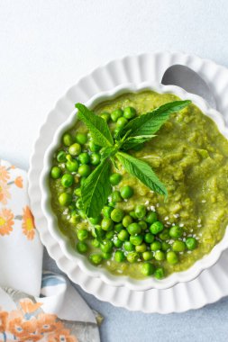 Parlak yeşil bezelye ve brokoli püresi bir kâseyi doldurur, taze nane ve bezelye ile süslenir, öğle veya akşam yemeği için mükemmel taze ve sağlıklı bir çorba sergiler.