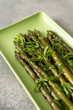 Taze ızgara kuşkonmaz üzerine doğranmış yeşil soğan modern bir mutfakta yeşil bir tabakta duruyor. Bu canlı şey sağlıklı yemek ve taze malzemeler sergiliyor.