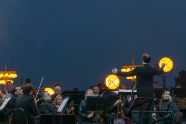지휘자 배경에 공연 자와 함께 심포니 오케스트라 지휘.