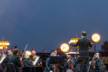 지휘자 배경에 공연 자와 함께 심포니 오케스트라 지휘.