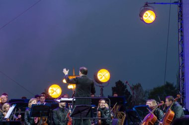 지휘자 배경에 공연 자와 함께 심포니 오케스트라 지휘.