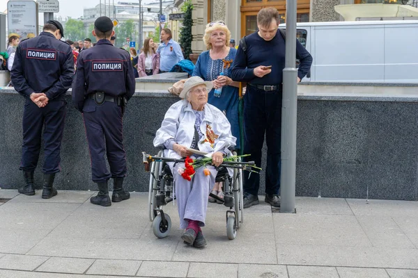 Moskova, Rusya - 9 Mayıs 2019: Elinde çiçek tutarken tekerlekli sandalyede oturan yaşlı kadın