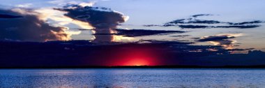 Dramatik bir fırtınalı gökyüzü gündoğumu deniz manzarası. Mavi gökyüzü ve Kızıl Güneş kızdırma, featuting ile bir örs bulut oluşumu deniz üzerinde su su yansımaları ile