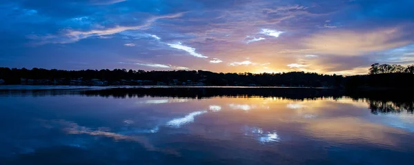 Huzurlu mavi gökyüzü ve turuncu güneş bulutlu gündoğumu deniz manzarası üzerinde deniz suyu su yansımaları ile kızdırma. Queensland, Avustralya.