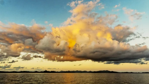 Beauty in nature. This unique tropospheric skyart photography is from the Australian East Coast.  Yellow and grey cumulonimbus formation in an atmospheric cerulean blue sky. Sunset display over water and through cloud.