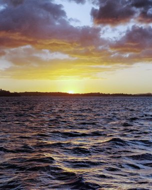 Avustralya yaz deniz manzarası, bir okyanus dalgaları ile waterscape, turuncu ve sarı renkli günbatımı öncelikle cumulus bulutları karşı köpüklü kıyı okyanus sularında yansıyan bir soluk mavi gökyüzü ile.