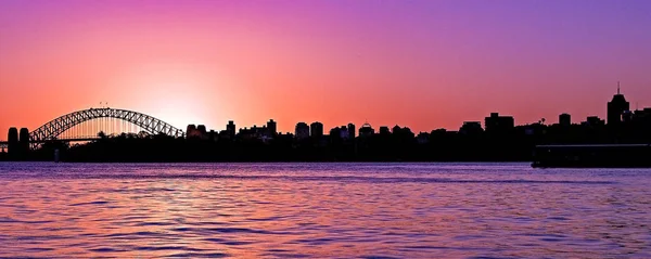 悉尼海港大桥和城市天际线的特色是和平的洋红色彩色 Nimbostratus 云日落海景在平静的反射海洋水域 与柔和的粉红色有色自然天空反射在宁静的海滨海港 澳大利亚 — 图库照片