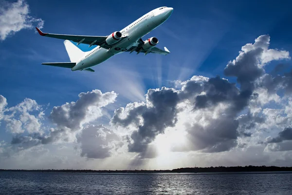 Jet aircraft departing Mascot Airport flyng over Botany Bay in a vibrant blue sky, with bright white coloured Sun Rays and cumulonimbus clouds. Sydney, New South Wales, Australia.