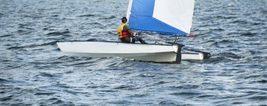 Çocuk Yelken küçük katamaran yelkenli bir iç su yolu üzerinde mavi ve beyaz yelken ile.