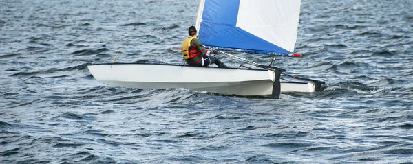 Çocuk Yelken küçük katamaran yelkenli bir iç su yolu üzerinde mavi ve beyaz yelken ile.