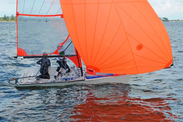 Dos niños navegando un bote de carreras con un gran spinnaker de color naranja completamente desplegado . —  Fotos de Stock
