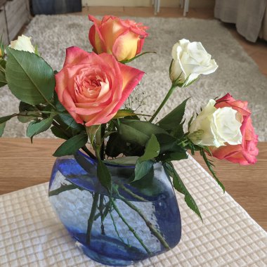 Doğadaki güzellik. Beyaz sehpa örtüsünün üzerinde şeffaf mavi vazoda duran pembe ve beyaz güller. İçeride. Avusturalya. 