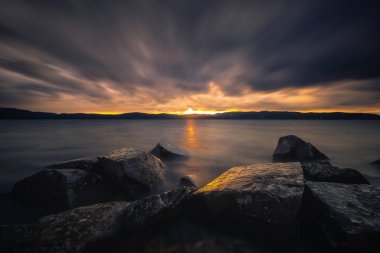 Gün batımı ışık ve Norveç'te Jonsvatnet gölün akşam ruh hali. Trondheim alan. Uzun süreli pozlama. Sonbaharın bulutlu ve rüzgarlı gün.