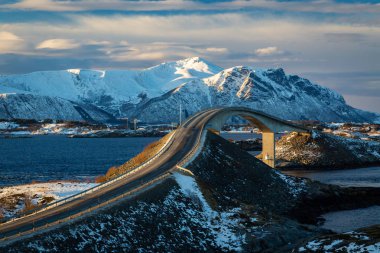 Atlantic Ocean Road - kış güneşli günde Atlanterhavsvegen. Denizin üzerinde ünlü yüksek köprü adı Storseisundbrua ve karlı dağlarda güzel bir ufuk.