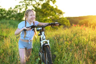 happy child girl with a bicycle goes through a meadow. She enjoy nature. Outdoor sport activity.