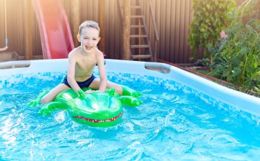 Evdeki havuzda şişme timsah yüzen çocuk. Çocuklarla yaz tatili. Yüzme yardımcıları ve çocuklar için giysi. Su oyuncakları. Renkli salda yüzen küçük çocuk.