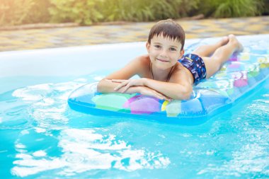 Evinin havuzunda şişme yüzen bir çocuk. Çocuklarla yaz tatili. Yüzme yardımcıları ve çocuklar için giysi. Renkli salda yüzen küçük çocuk.