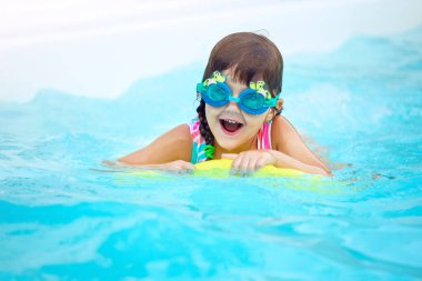 Çocuk tropikal tatil köyü havuzunda yüzmeyi öğreniyor. Çocuklar yüzmeyi öğrenir. Küçük çocuklar için egzersiz ve eğitim. Spor kulübünde sörf tahtası olan küçük bir kız. Yüzen bebek ya da bebek.