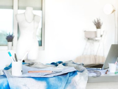 Dikiş ve örgü aletleri, aksesuarlar, terzi mankeni, dizüstü bilgisayar, çizimler olan bir elbise yapma stüdyosu. Keten kumaşa nakledilmek üzere ayarlandı. Bir sürü boşluk.