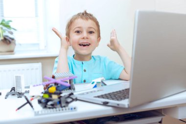 Neşeli hoş çocuk modern mühendislik okurken robot aletlerini test ediyor. O, işinden çok memnun. Çevrimiçi eğitim, E-öğrenme kavramı, dizüstü bilgisayarla mesafe iletişimi