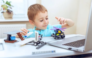 Robot tutan neşeli, küçük bir çocuk. O, işinde çok memnun, masada oturuyor ve inşa ediyor. Çevrimiçi eğitim, E-öğrenme kavramı,