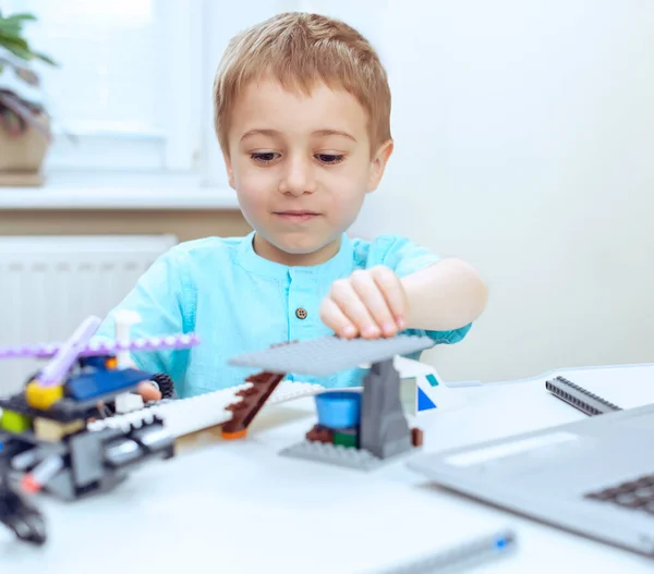 preschool boy is try hard constructing a robotic device while doing his home assignment. Online education, E-learning concept, distance communication with laptop