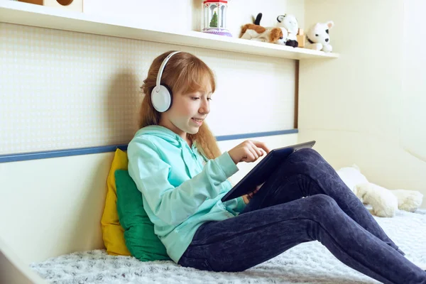 the girl sits on the bed in the room, listens to audio or video lessons at home. Online education, E-learning concept, distance communication with laptop
