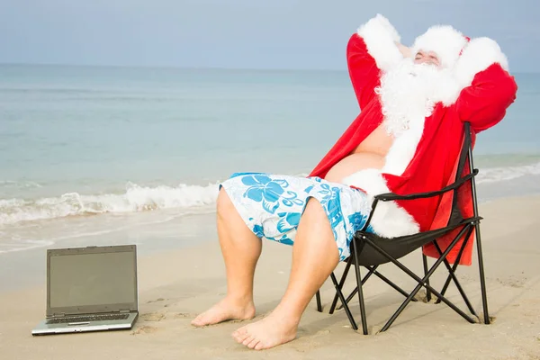 Funny Santa on the beach working on laptop.