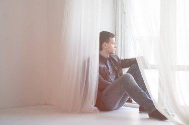 Pencere pervazına üzerinde oturan genç yakışıklı adam. Dinlenmek ve rahatlamak
