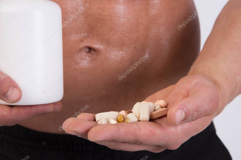 Young muscular guy. Sports nutrition. Accepts tablets after training. White background.