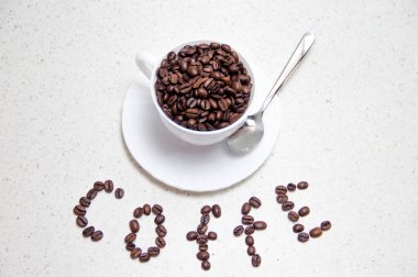 Beyaz bir fincankahve çekirdekleri. Dağınık kahve çekirdekleri