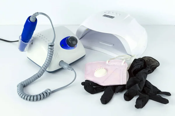 Utensili e attrezzature per manicure. Una maschera medica e guanti di gomma si trovano accanto alla macchina manicure . — Foto Stock