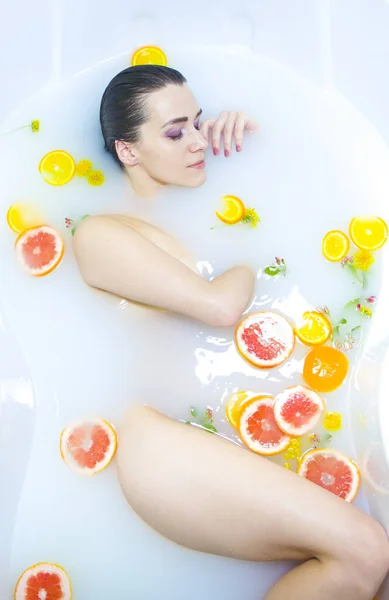 Girl in a milk bath, Spa treatments. An attractive girl takes a bath with milk and flowers. Spa treatments for skin rejuvenation