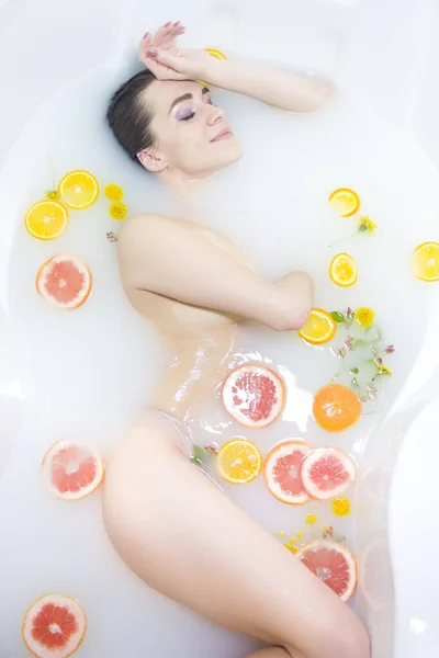 Girl in a milk bath, Spa treatments. An attractive girl takes a bath with milk and flowers. Spa treatments for skin rejuvenation