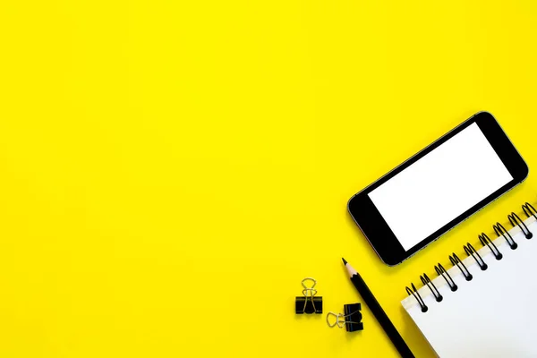  Telefon, defter kalem sarı arka plan ile. Üstten görünüm.