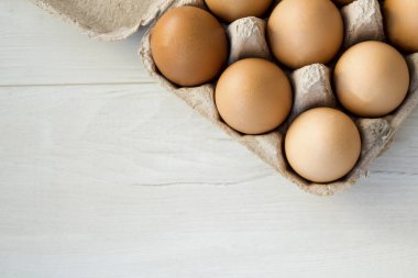 Beyaz ahşap arka planda yumurta kutusundaki çiğ tavuk yumurtalarının yakın plan görüntüsü.