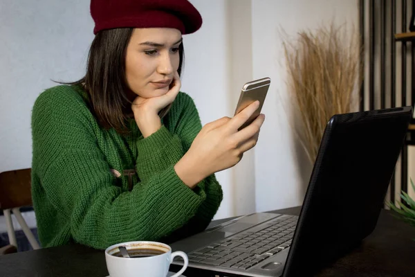  Bir dizüstü bilgisayar ile bir kafede Smartphone kullanan genç kadın.